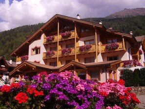A multi-story hotel with balconies adorned with flowers, set against a mountainous backdrop. - Gran Zebru (Pejo)