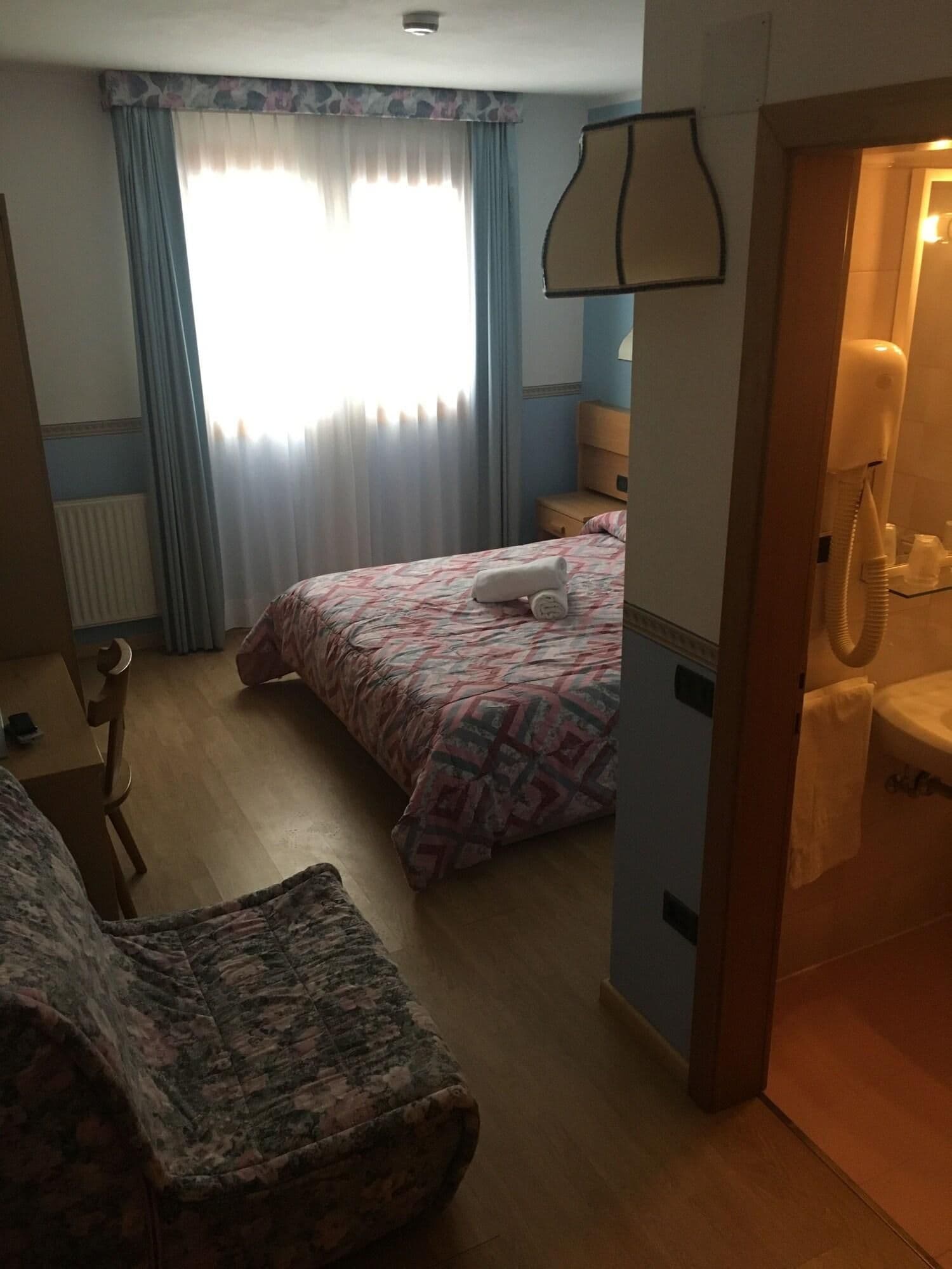 Ein Hotelzimmer mit einem Bett, einem Sessel, einem Schreibtisch, einem Telefon und einem Badezimmer.