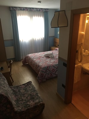 Una habitación de hotel con cama, sillón, escritorio, teléfono y baño.
