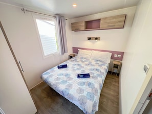 A bedroom with a bed, a window with curtains, a bedside table, and a wall-mounted shelf. - Happy Camp in Camping La Masseria (Gallipoli)