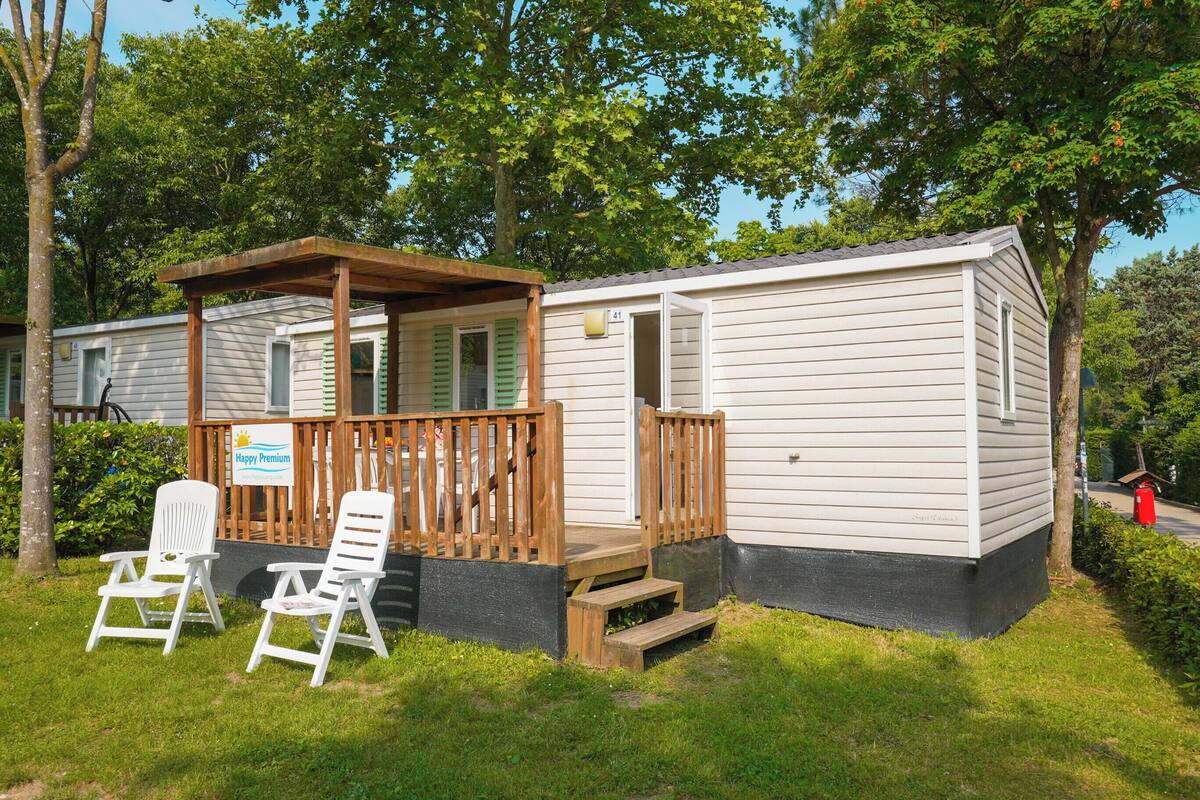 A mobile home with a porch, two white lawn chairs, and a 'Happy Premium' sign.