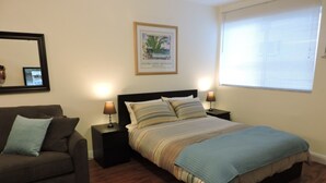 A bedroom with a bed, a nightstand, a lamp, a framed picture on the wall, a window, and a couch. - Seabreeze Beachside Studios by ValGal (Hollywood)