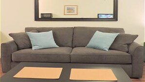 A living room with a grey sofa, two light blue cushions, and a black coffee table with two tan placemats. - Seabreeze Beachside Studios by ValGal (Hollywood)