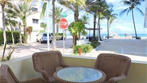 A balcony with wicker furniture, a stop sign, and a view of the beach and ocean. - Seabreeze Beachside Studios by ValGal (Hollywood)