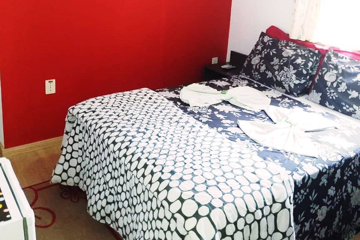 Un dormitorio con una pared roja, una cama con colcha estampada y un cuadro enmarcado sobre la cama.
