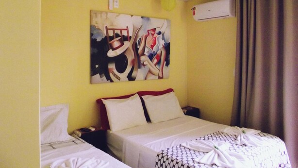 A hotel room with two beds, a painting on the wall, an air conditioning unit, and a curtain. - Pousada Tonapraia (Florianópolis)