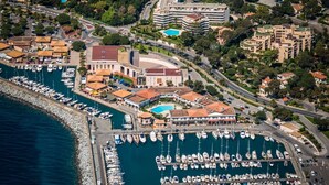 An aerial view of a marina with numerous boats docked, surrounded by residential buildings and a large hotel with a swimming pool. - Best Western La Marina (Saint-Raphael)
