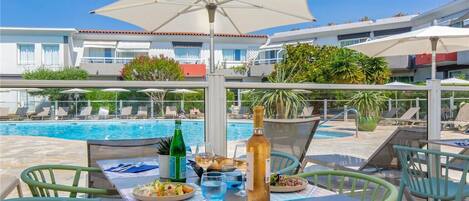 A poolside dining area with a table set for two, a bottle of wine, and a glass of water.
