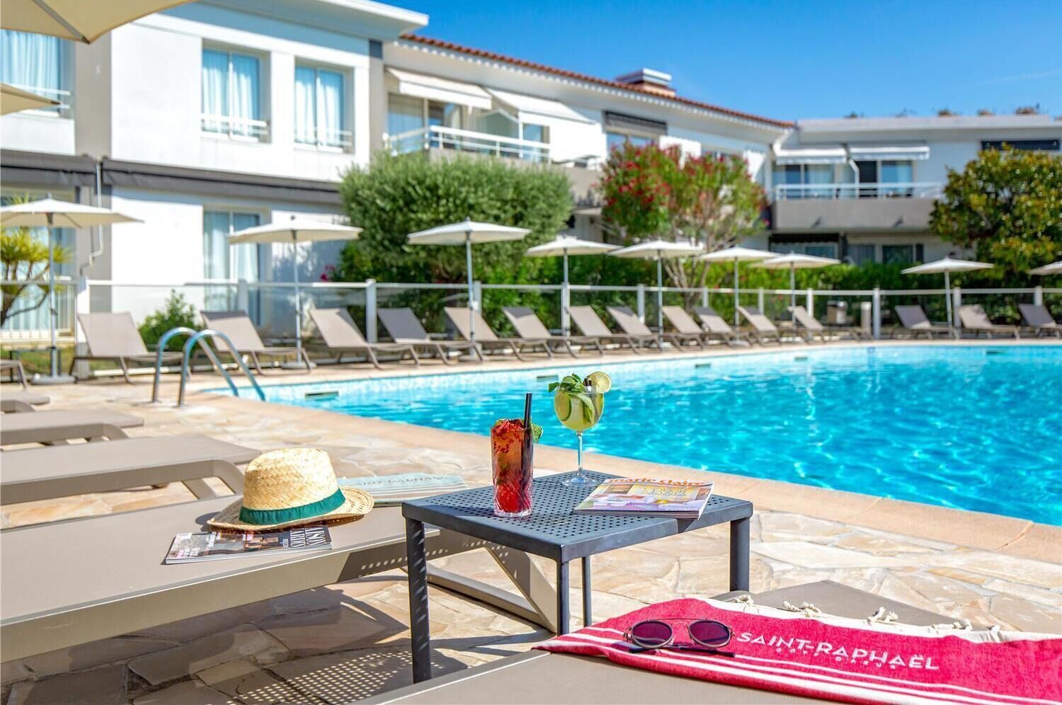 A poolside area with lounge chairs, a table with a drink, a hat, and a towel with the brand name.