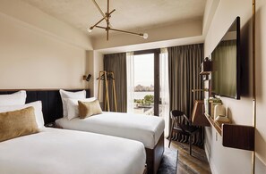 Habitación de hotel con dos camas, un ventanal con cortinas, un televisor montado en la pared y vistas a la ciudad.