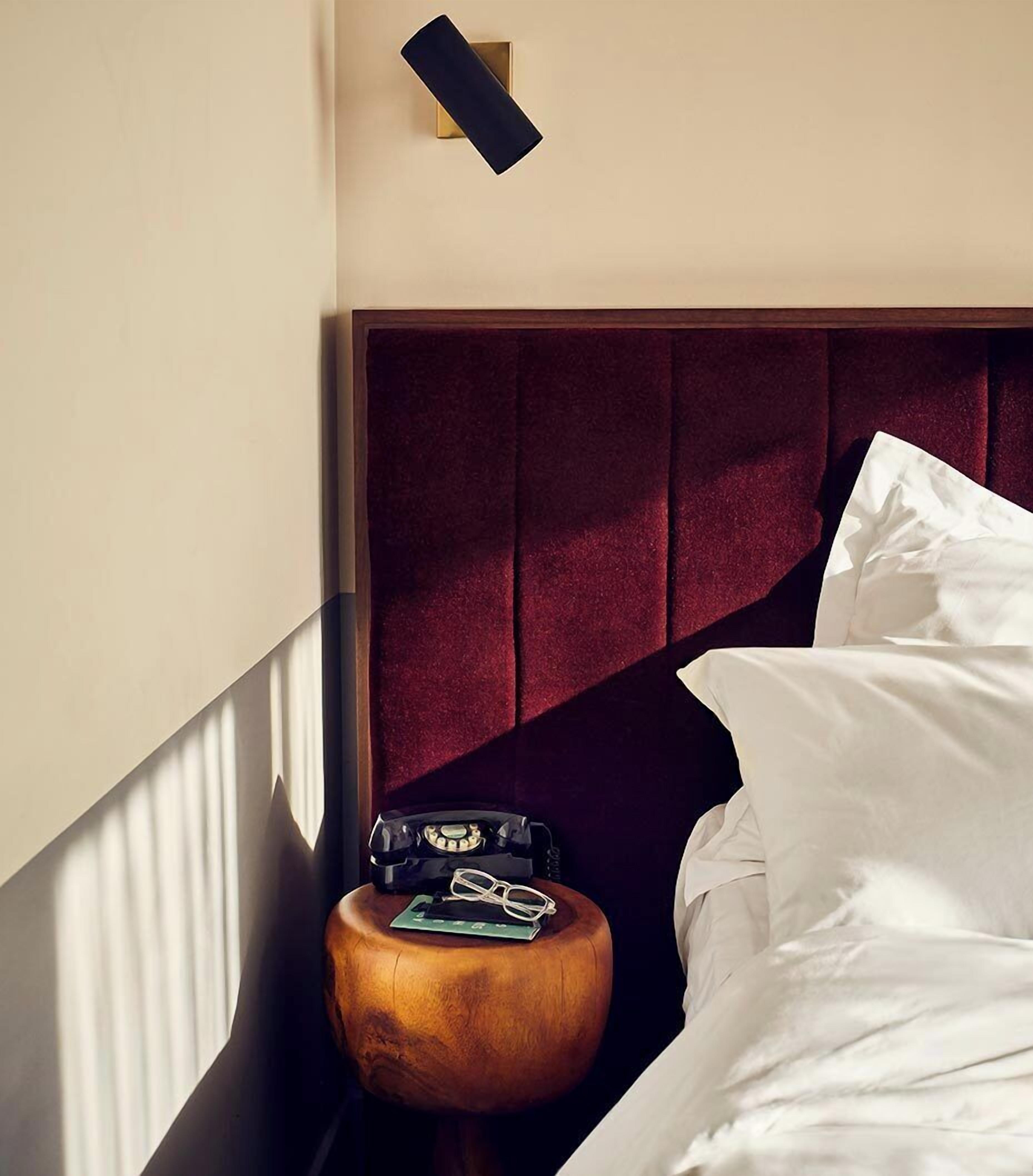 Una habitación de hotel con una mesita de noche de madera, un teléfono rotativo clásico y una cama bien hecha con ropa blanca.