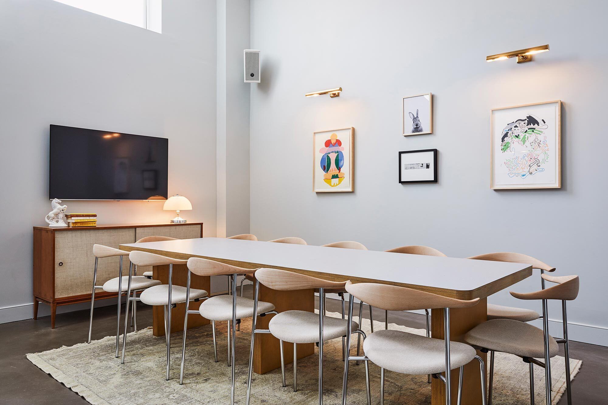 Una sala riunioni moderna con un lungo tavolo, sei sedie, un televisore e diverse opere d'arte incorniciate alle pareti.