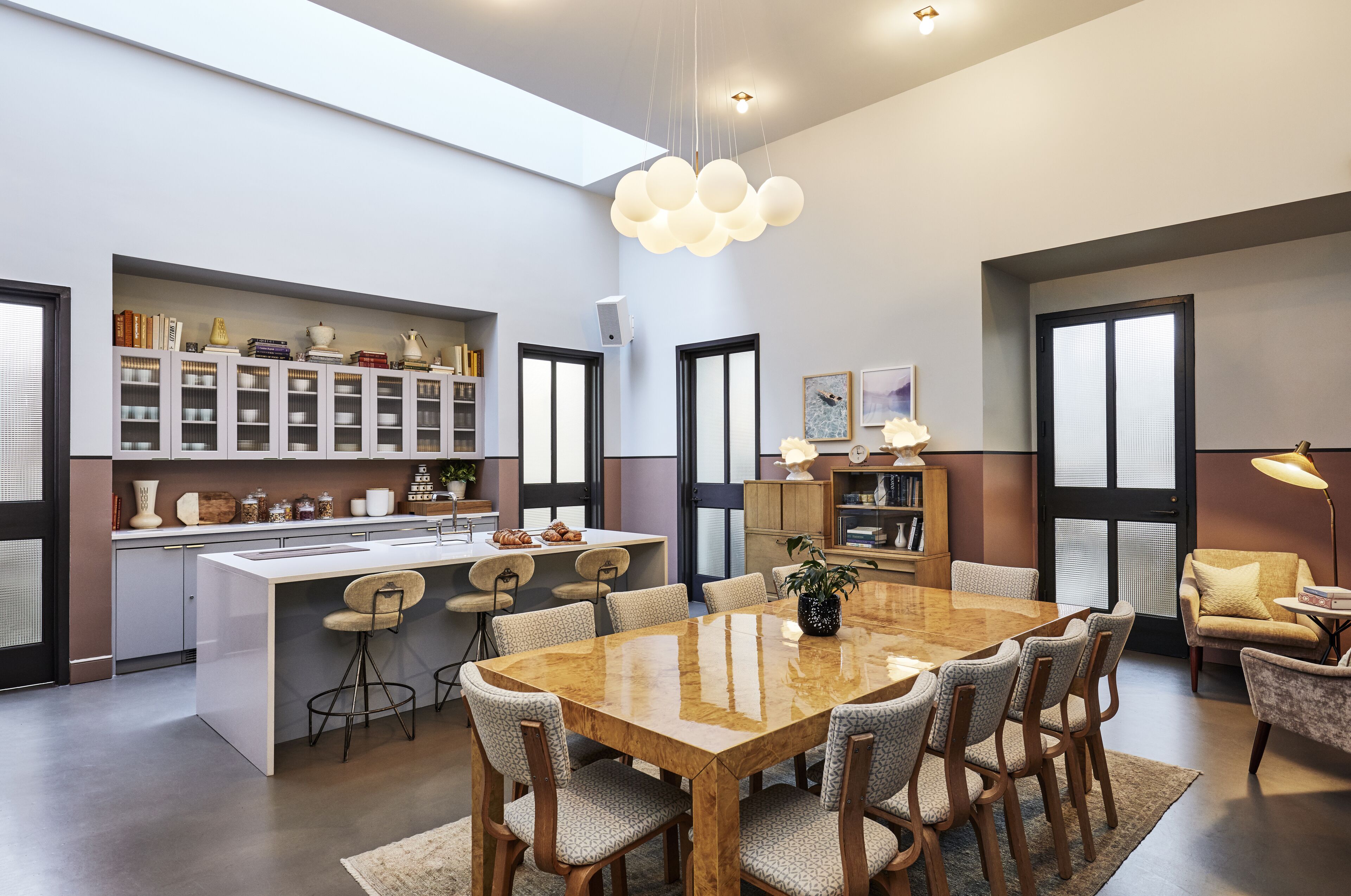 Une cuisine moderne dotée d’un îlot central, d’un coin repas avec une grande table et des chaises, et d’un espace détente avec un canapé et un fauteuil.