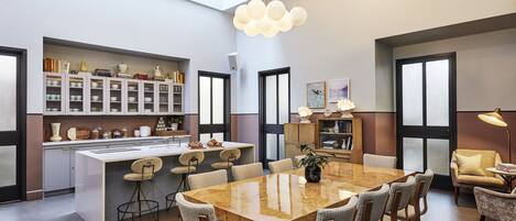 A modern kitchen with a central island, dining area with a large table and chairs, and a seating area with a sofa and armchair.