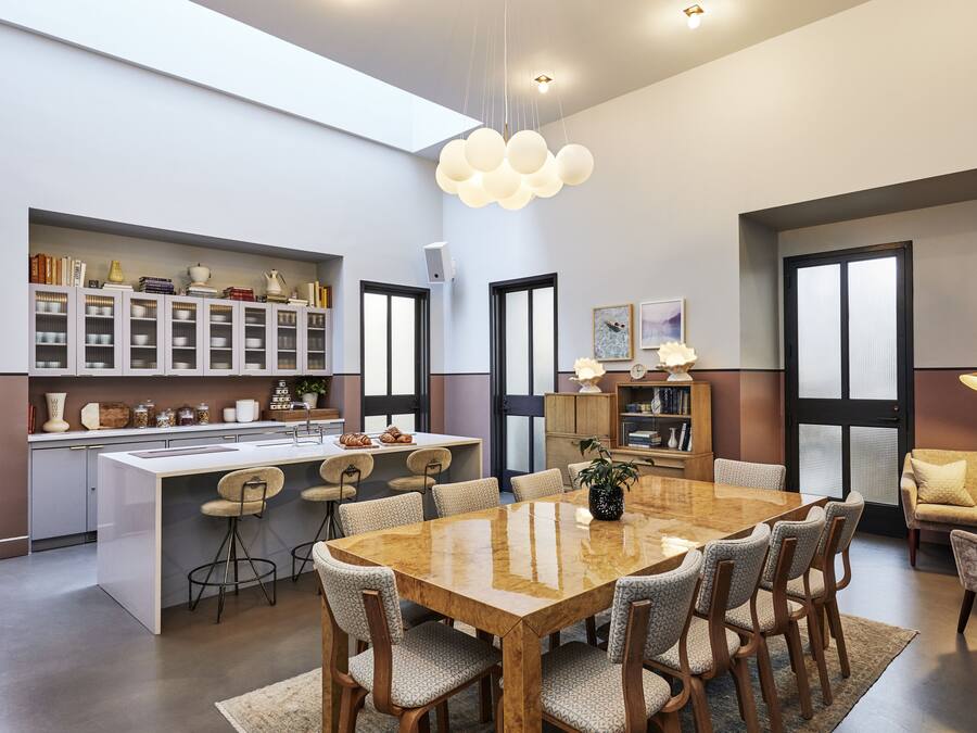 Une cuisine moderne dotée d’un îlot central, d’un coin repas avec une grande table et des chaises, et d’un espace détente avec un canapé et un fauteuil.