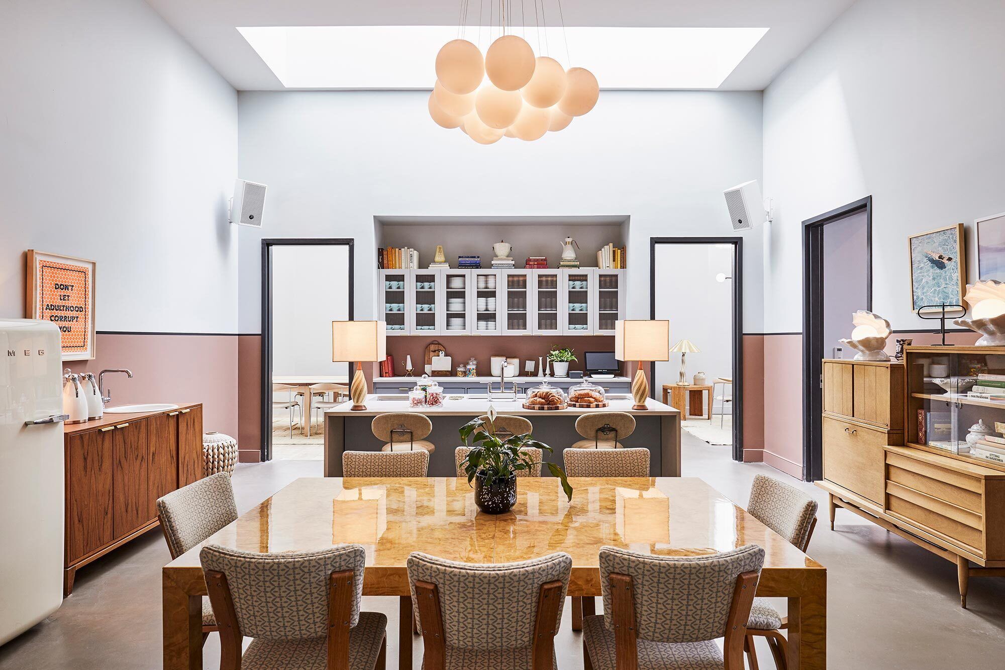 A modern kitchen with a central island, dining area with chairs, and a built-in bookshelf.