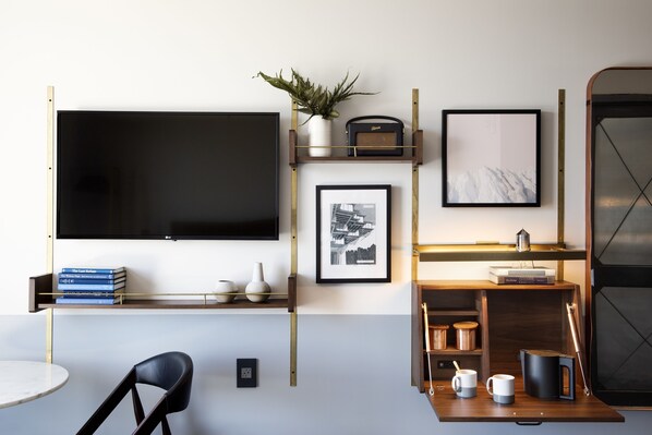 A modern living room with a flat-screen TV, books, a potted plant, framed pictures, and a coffee table with mugs and a kettle. - The Hoxton, Williamsburg (Brooklyn)