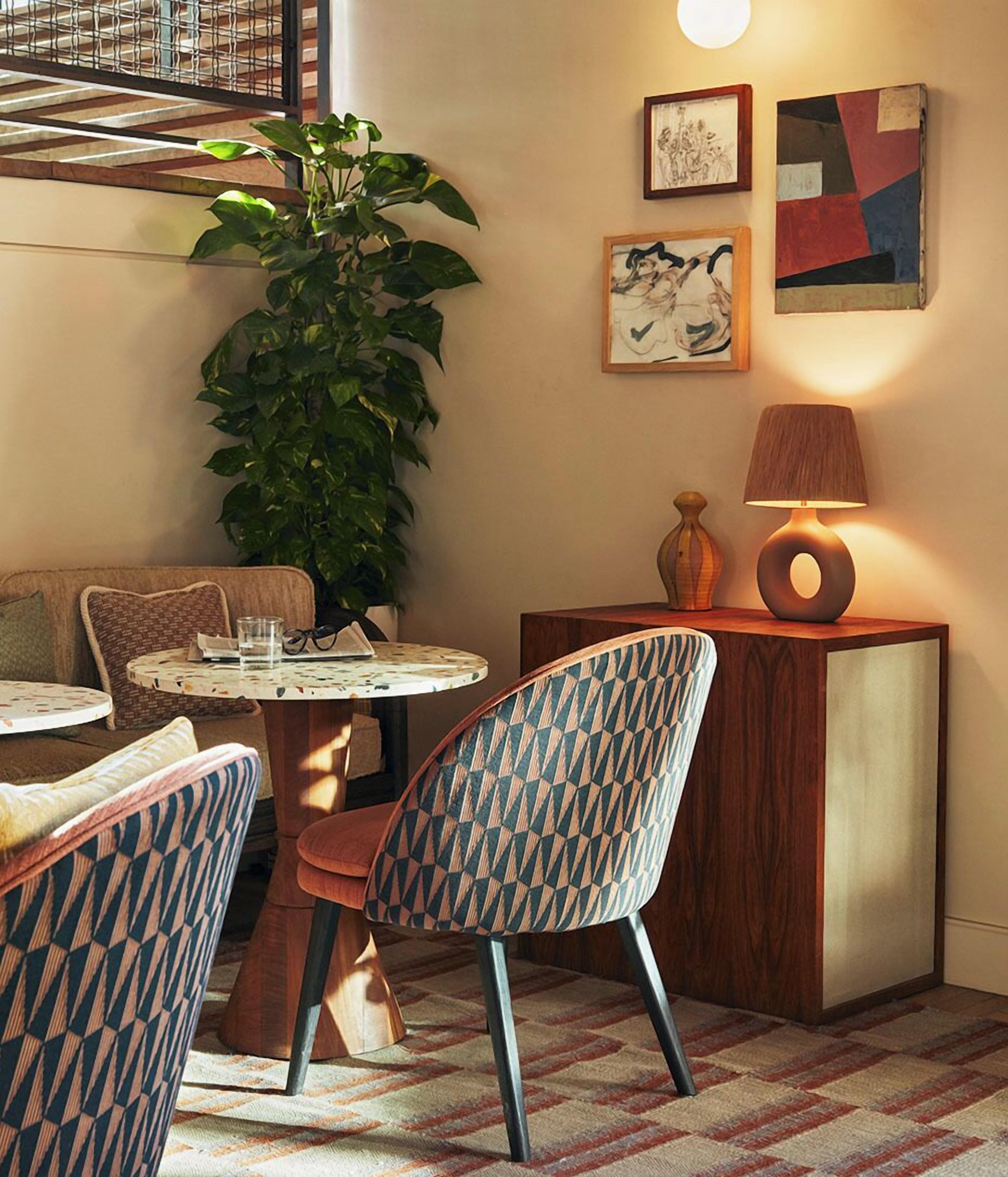 A cozy dining area with a round table, patterned chairs, a potted plant, and wall art.