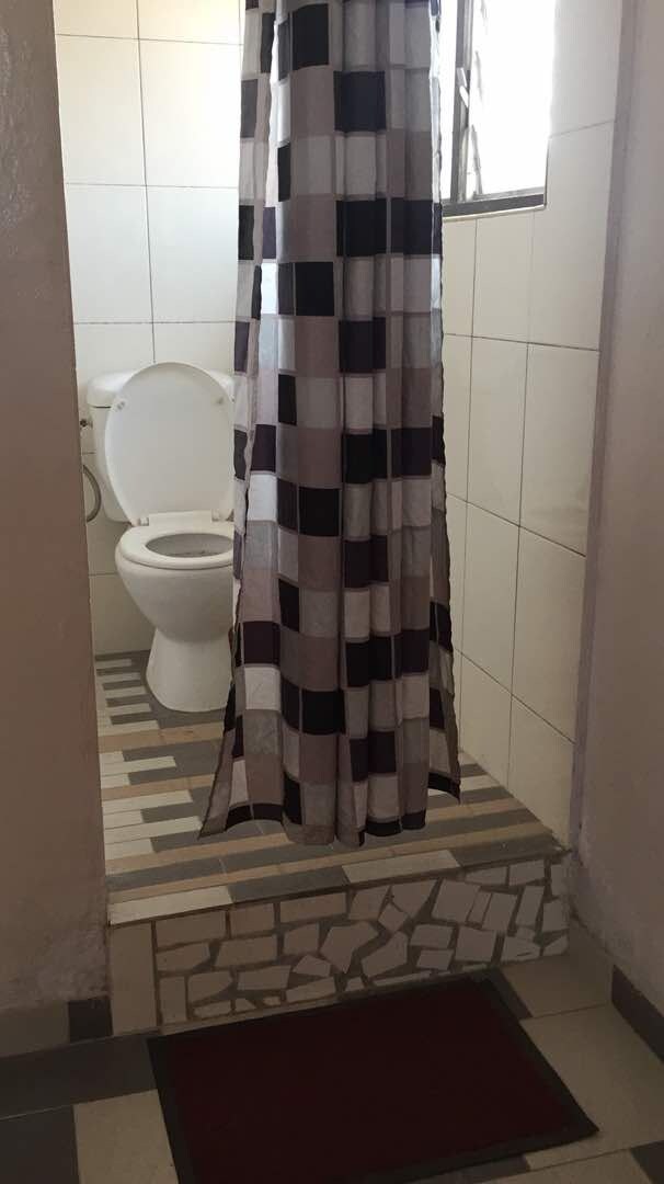 Un baño con piso de cerámica, inodoro blanco y cortina de ducha estampada.