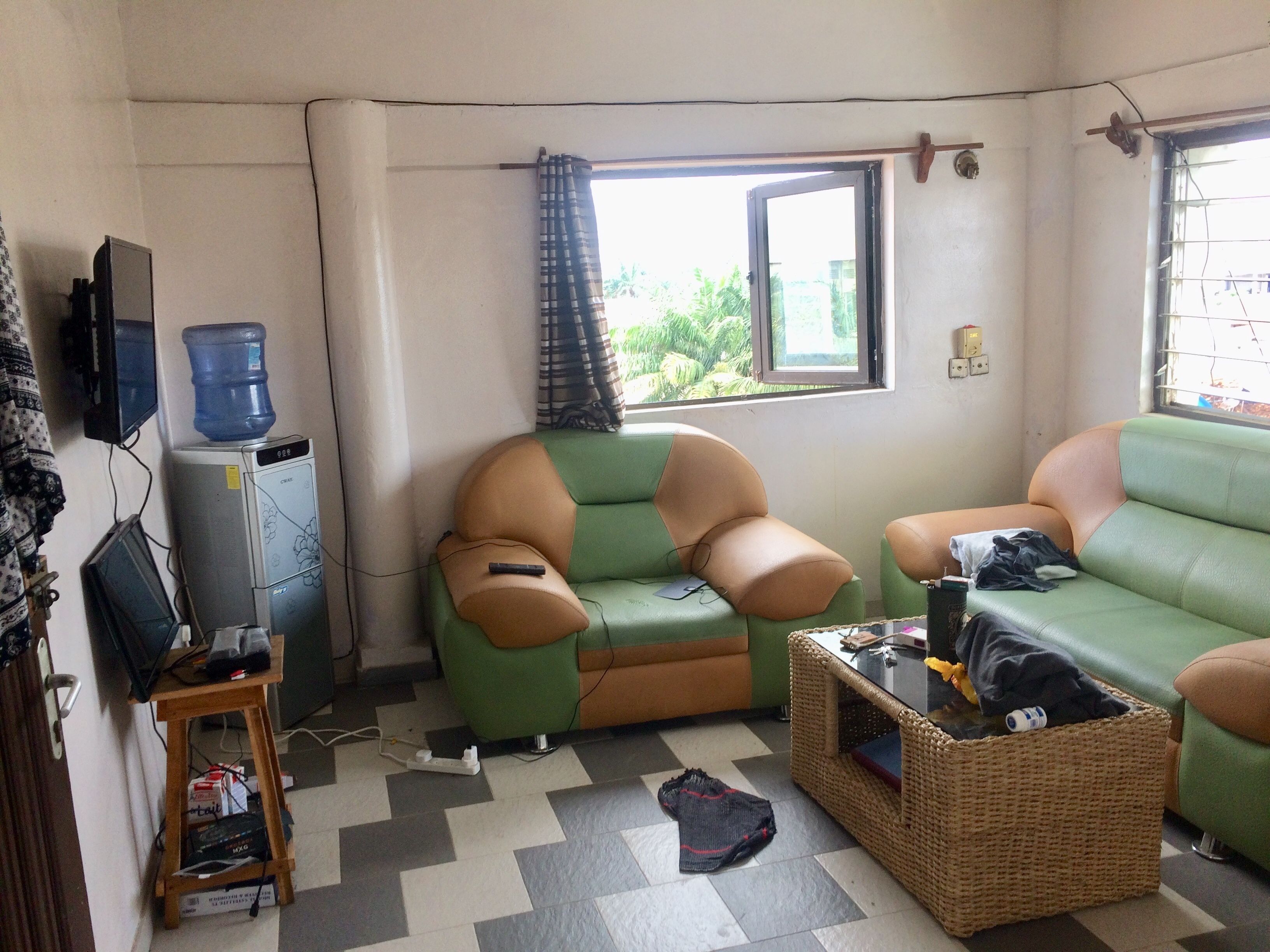 A small living room with a green and beige sofa, a television, a water dispenser, and a wicker basket.