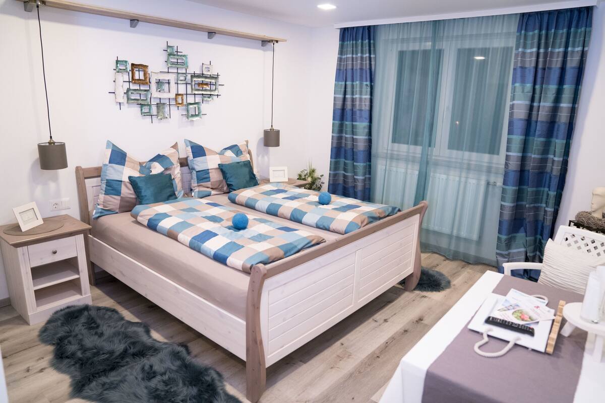A bedroom with a wooden bed, a nightstand, a fluffy rug, and a table with a remote and a magazine.