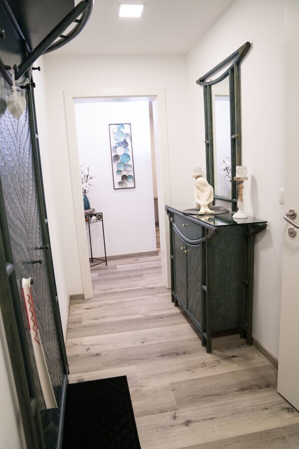 Un pasillo con piso de madera, un mueble negro con espejo y una puerta que da a otra habitación.