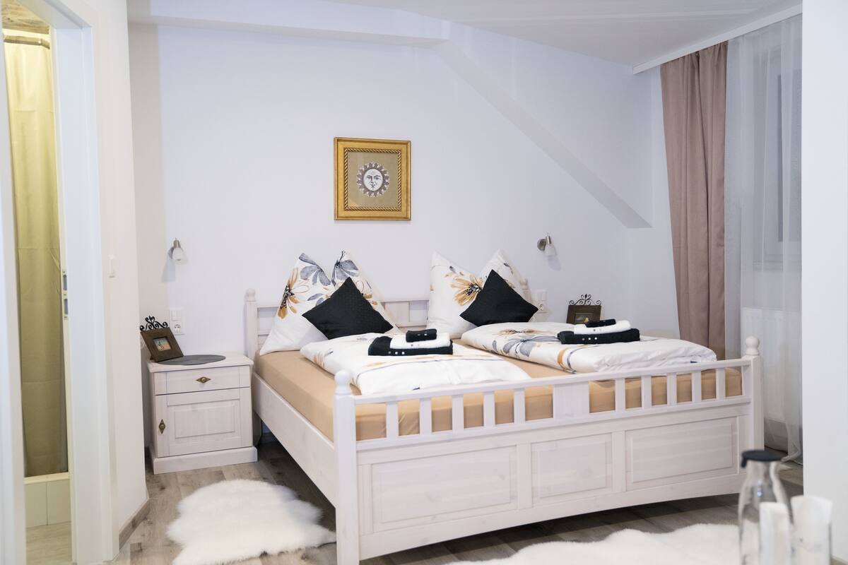 A bedroom with a white bed, two nightstands, a framed picture on the wall, and a white furry rug.