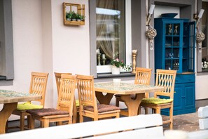 An outdoor dining area with wooden tables and chairs, a blue cabinet, and a window with curtains. - Pension & Restaurant La Amalia (Bad Sauerbrunn)
