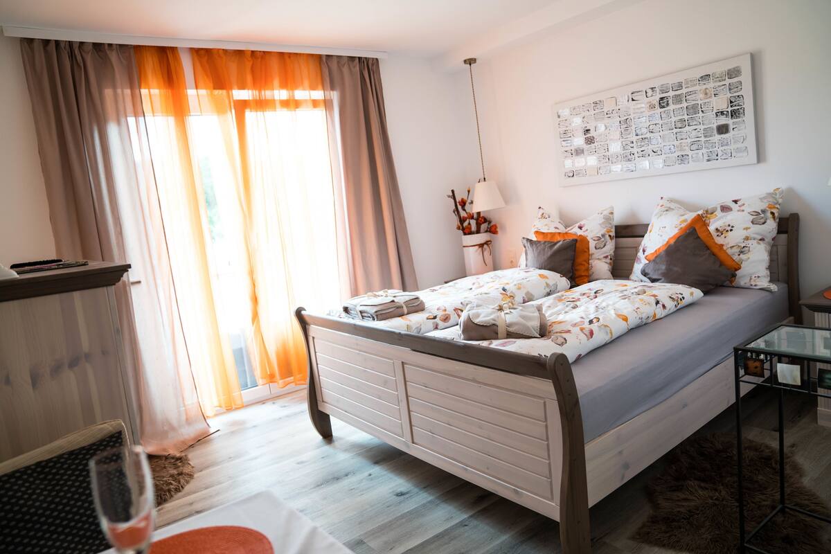 A bedroom with a bed, curtains, a wall art piece, and a lamp.