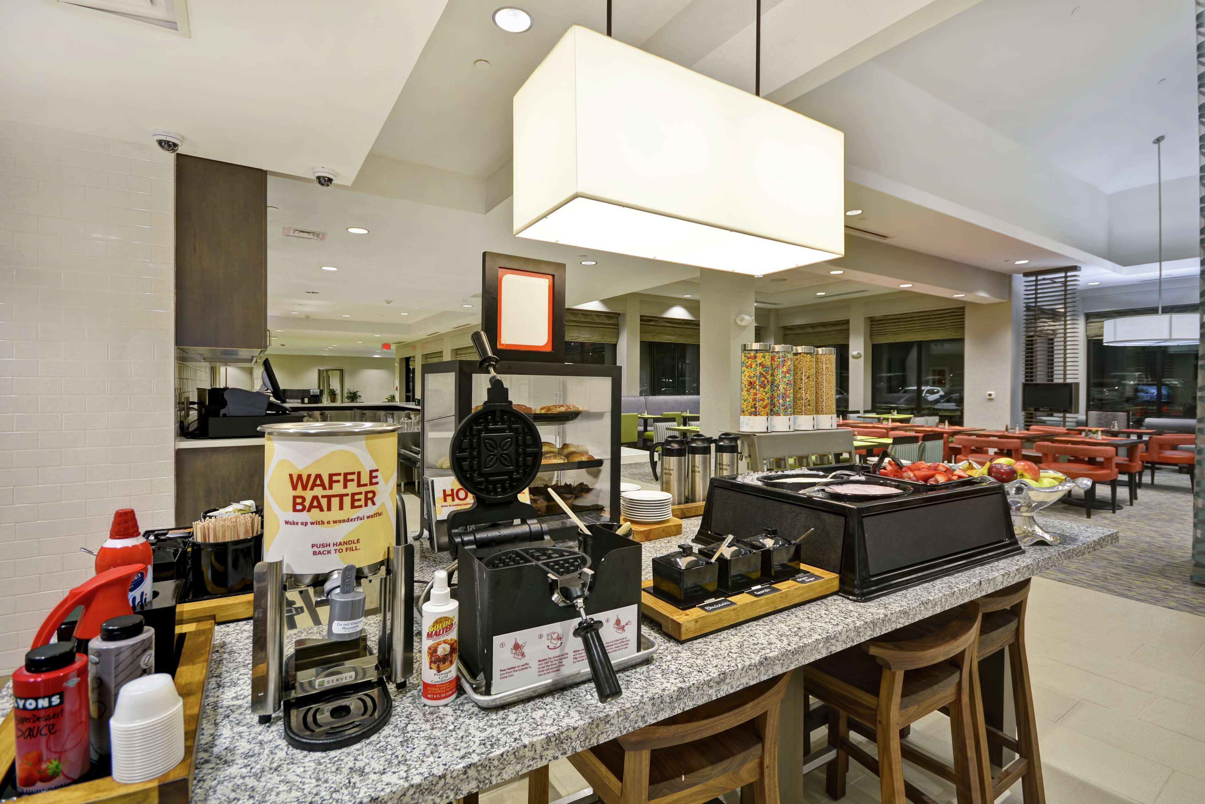 Un espace buffet proposant des distributeurs de pâte à gaufres, des machines à café et une variété de produits alimentaires.