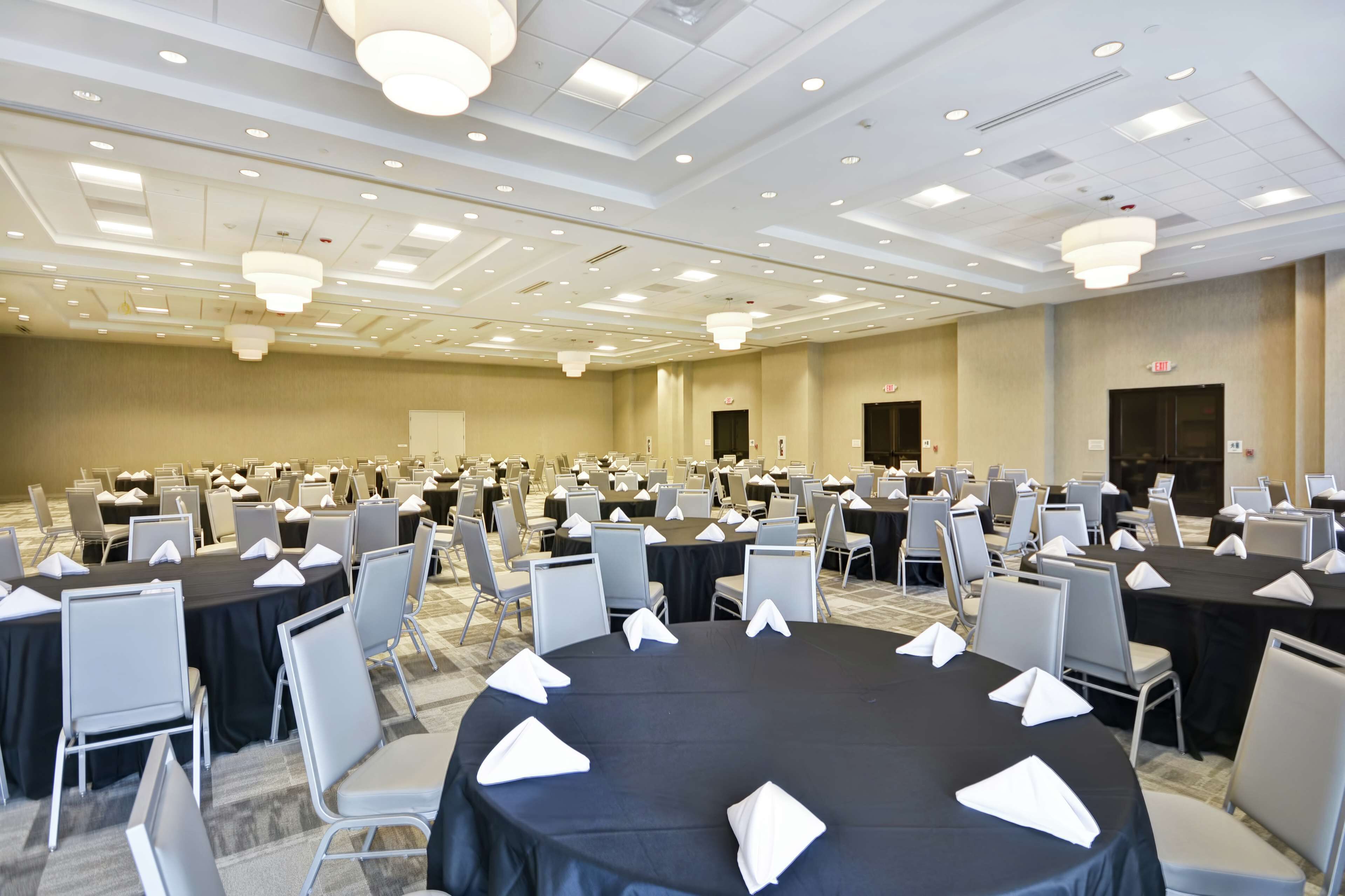 A large conference room with round tables, white chairs, and black tablecloths.