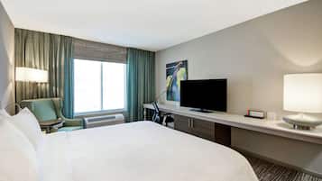 Habitació d'hotel amb un llit gran, un escriptori amb televisió de pantalla plana, una cadira i una finestra amb cortines.