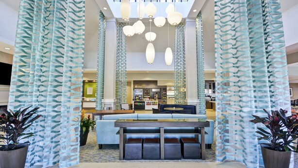 A spacious lobby with a central seating area, a coffee shop in the background, and a high ceiling with hanging lights. - Hilton Garden Inn Gastonia (Gastonia)