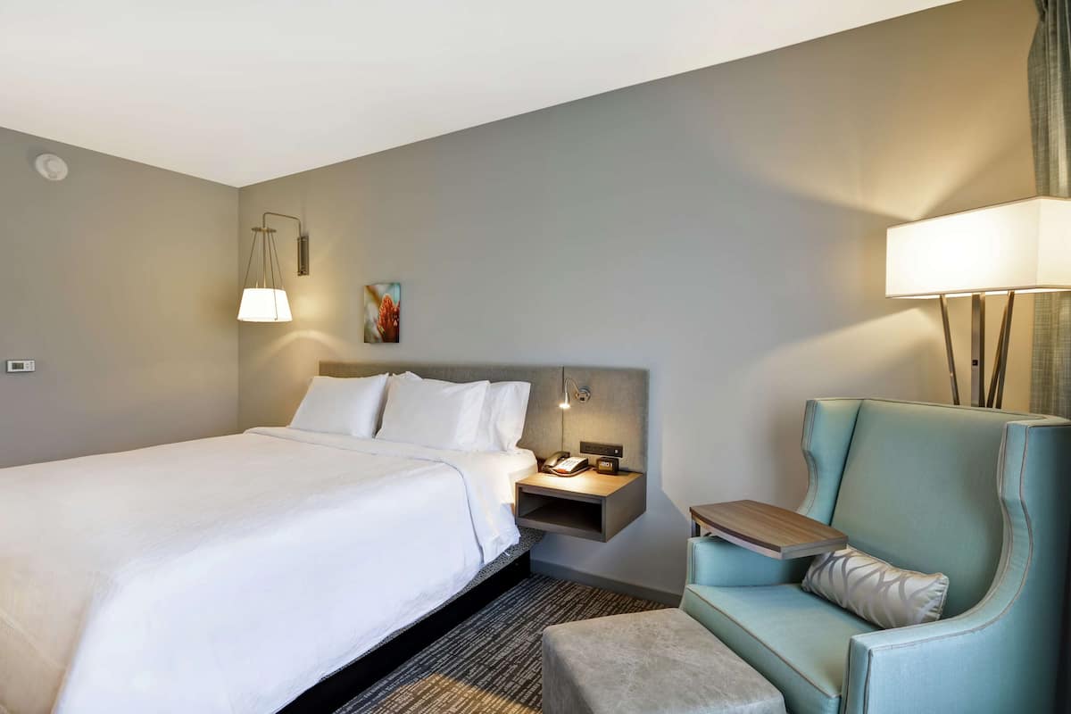 A hotel room with a bed, a nightstand with a lamp, a chair, and a small table.