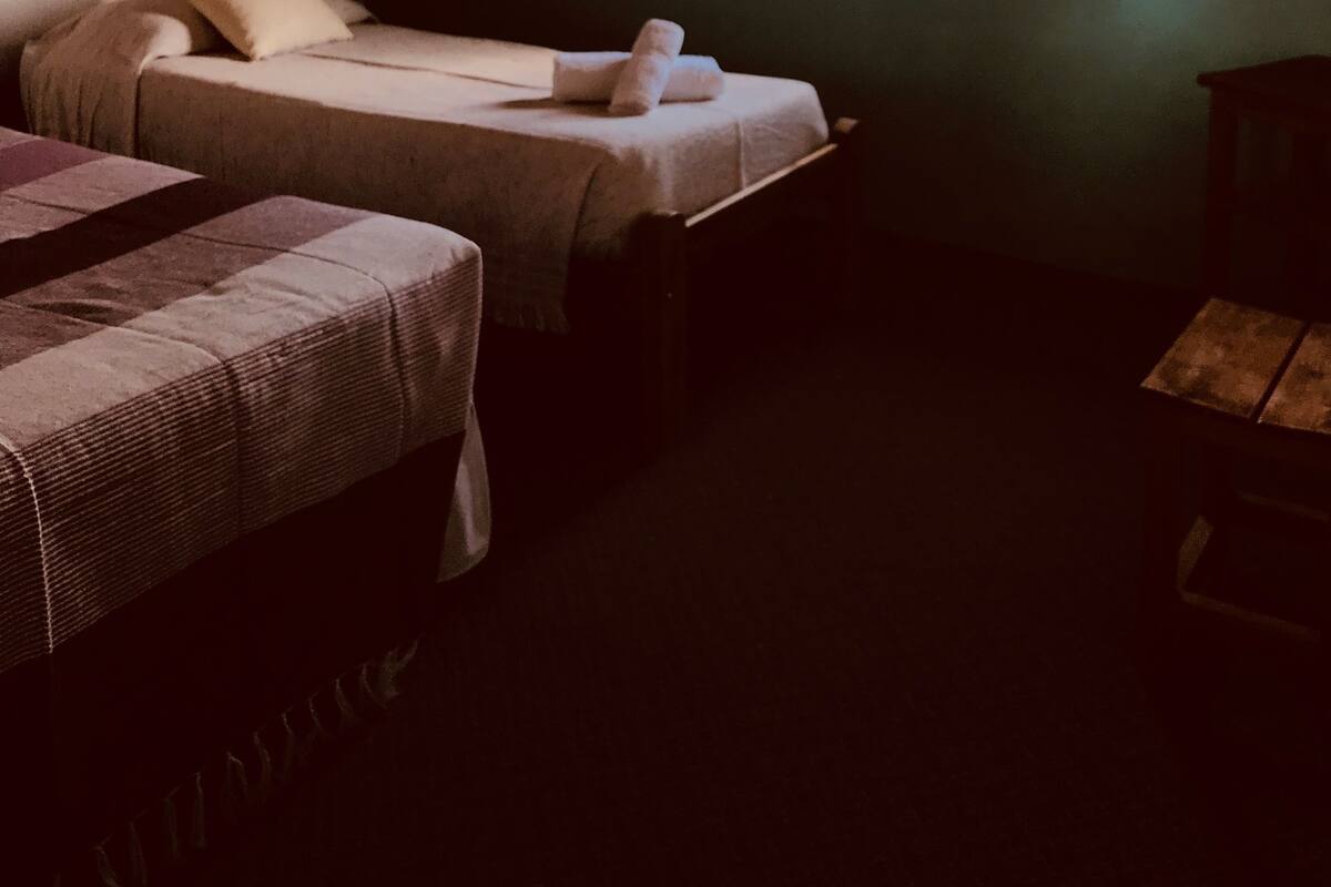 A room with two beds, a window with curtains, and a wooden ceiling.