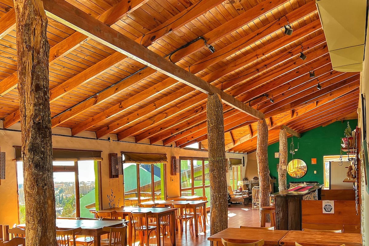A spacious dining area with wooden tables and chairs, high wooden ceilings, and large windows offering views of the outdoors.