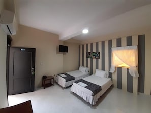 Ein Zimmer mit zwei Einzelbetten, einem kleinen Tisch, einem an der Wand befestigten Fernseher und einer Tür.