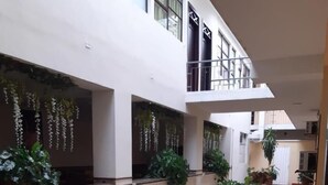 A corridor with potted plants, tiled flooring, and a white building with windows and a balcony. - Hotel El Andino (San José de Cúcuta)