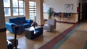A lobby with a blue sofa, a white armchair, a coffee table, a fan, and a potted plant. - Hotel El Andino (San José de Cúcuta)