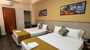 A hotel room with two beds, each with a white bedspread and a brown throw blanket. There are two paintings on the wall, a door, and a small table with a lamp. - Hotel El Andino (San José de Cúcuta)