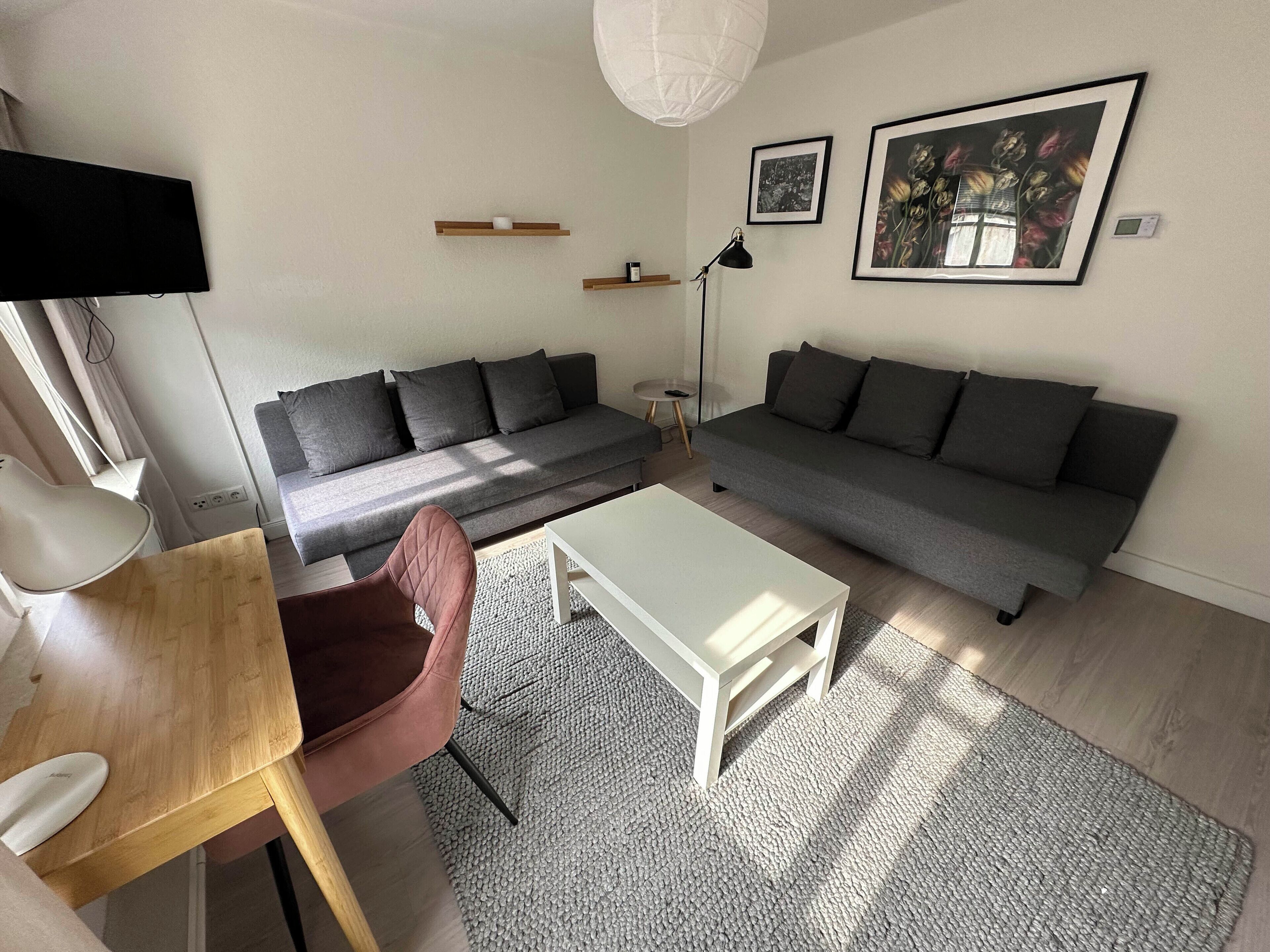 Ein modernes Wohnzimmer mit zwei grauen Sofas, einem weißen Couchtisch, einem Holznachttisch und einem grauen Teppich.