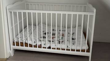 Een wit kinderbed met een stippenmatras in een kamer met schuine wanden en een kleine spiegel aan de muur.