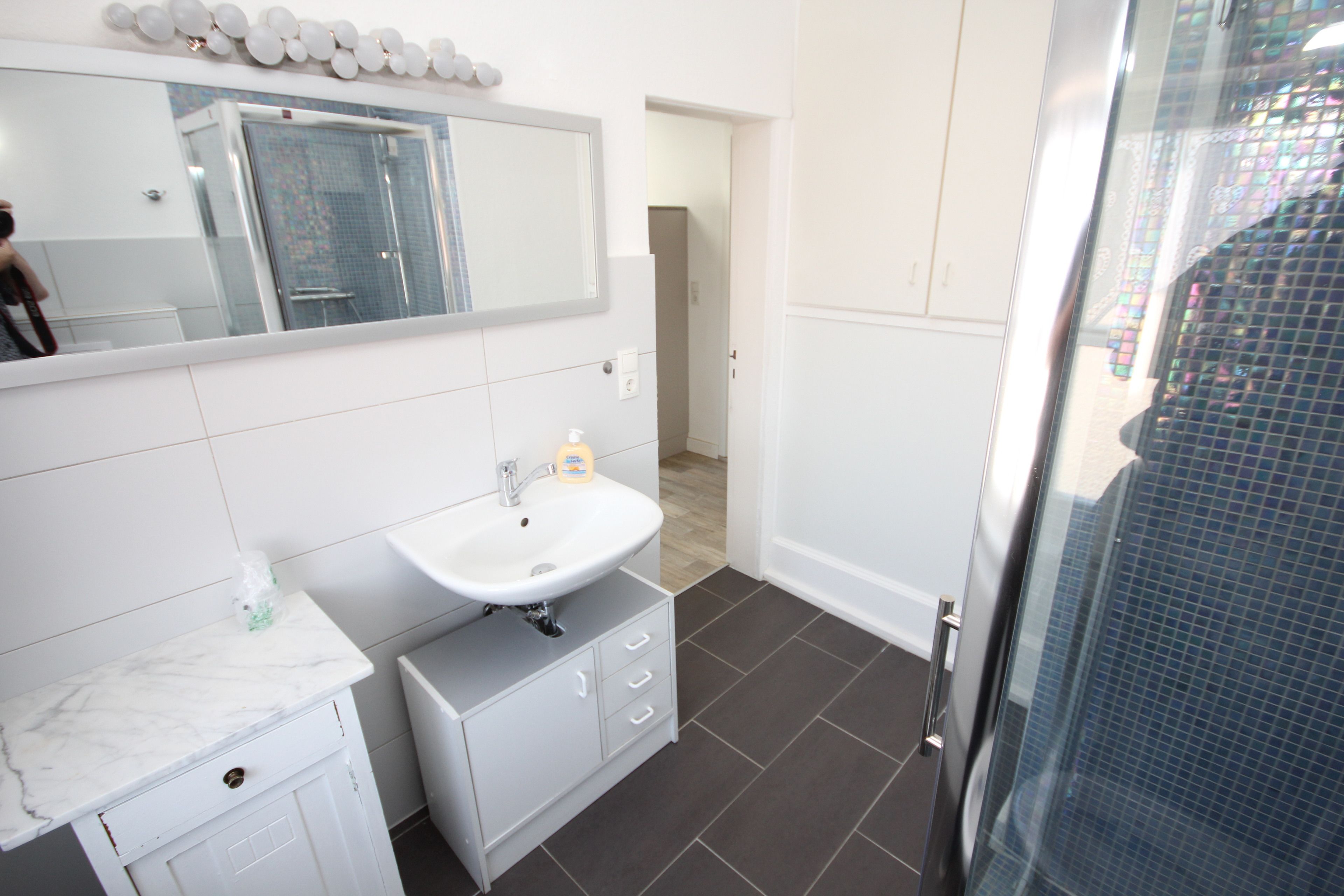 Une salle de bain avec un lavabo blanc, un miroir et un sol carrelé.