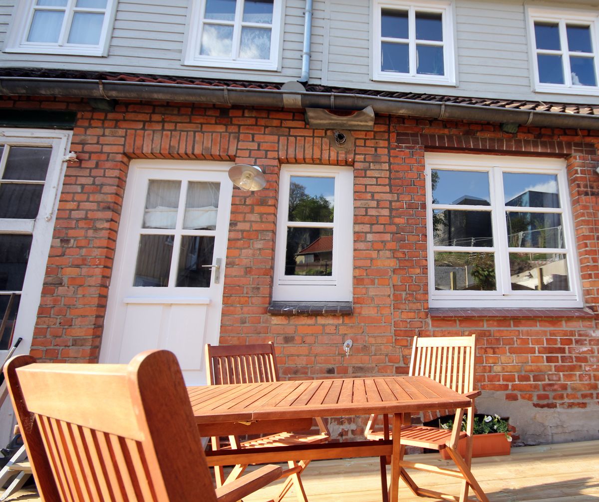 A brick house with two white-framed windows, a door, and a wooden table with chairs in front.