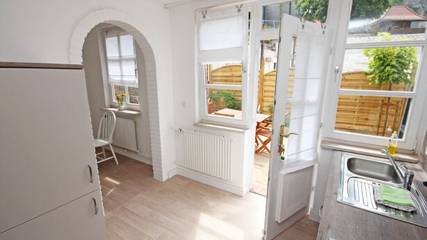 Eine Küche mit weißen Schränken, Holzboden, Heizkörper und Fenster mit Blick auf einen Garten.