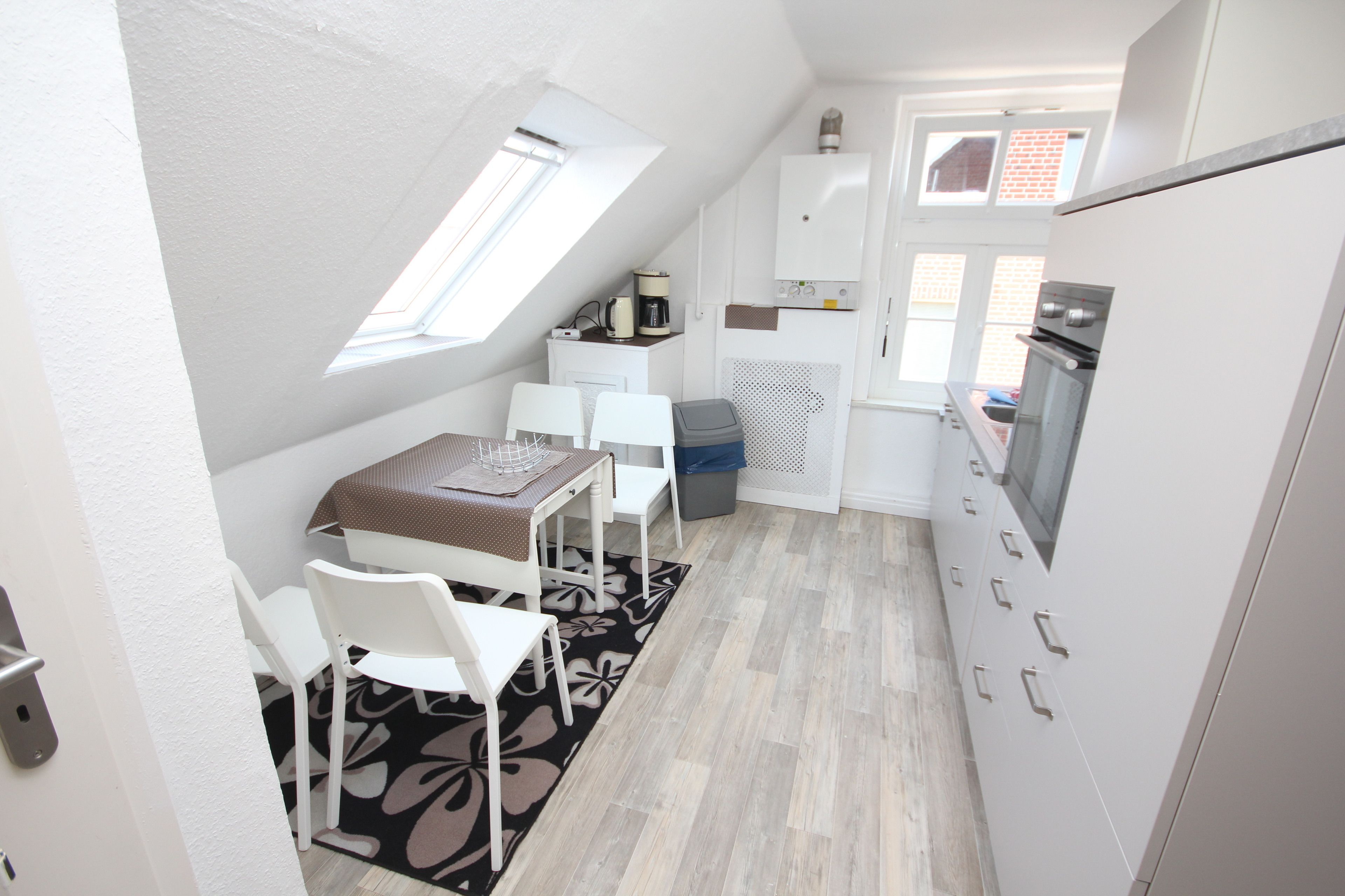 A compact kitchen with a dining area, a small table, and chairs. There is a window providing natural light, and a built-in oven is visible.