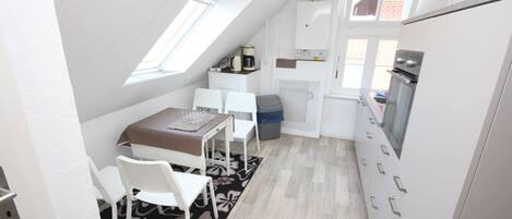 A compact kitchen with a dining area, a small table, and chairs. There is a window providing natural light, and a built-in oven is visible.