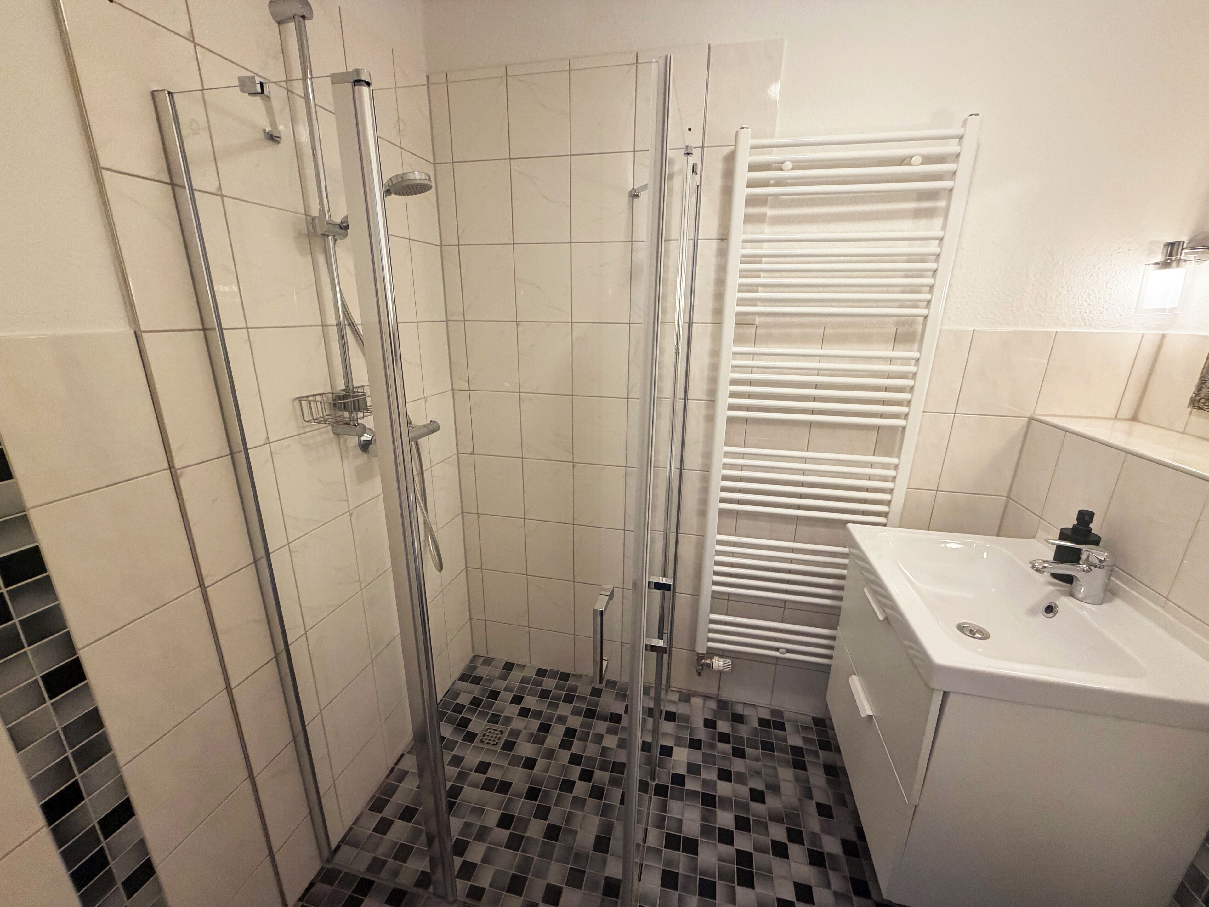 A modern bathroom with a shower enclosure, a white sink, and a tiled floor.