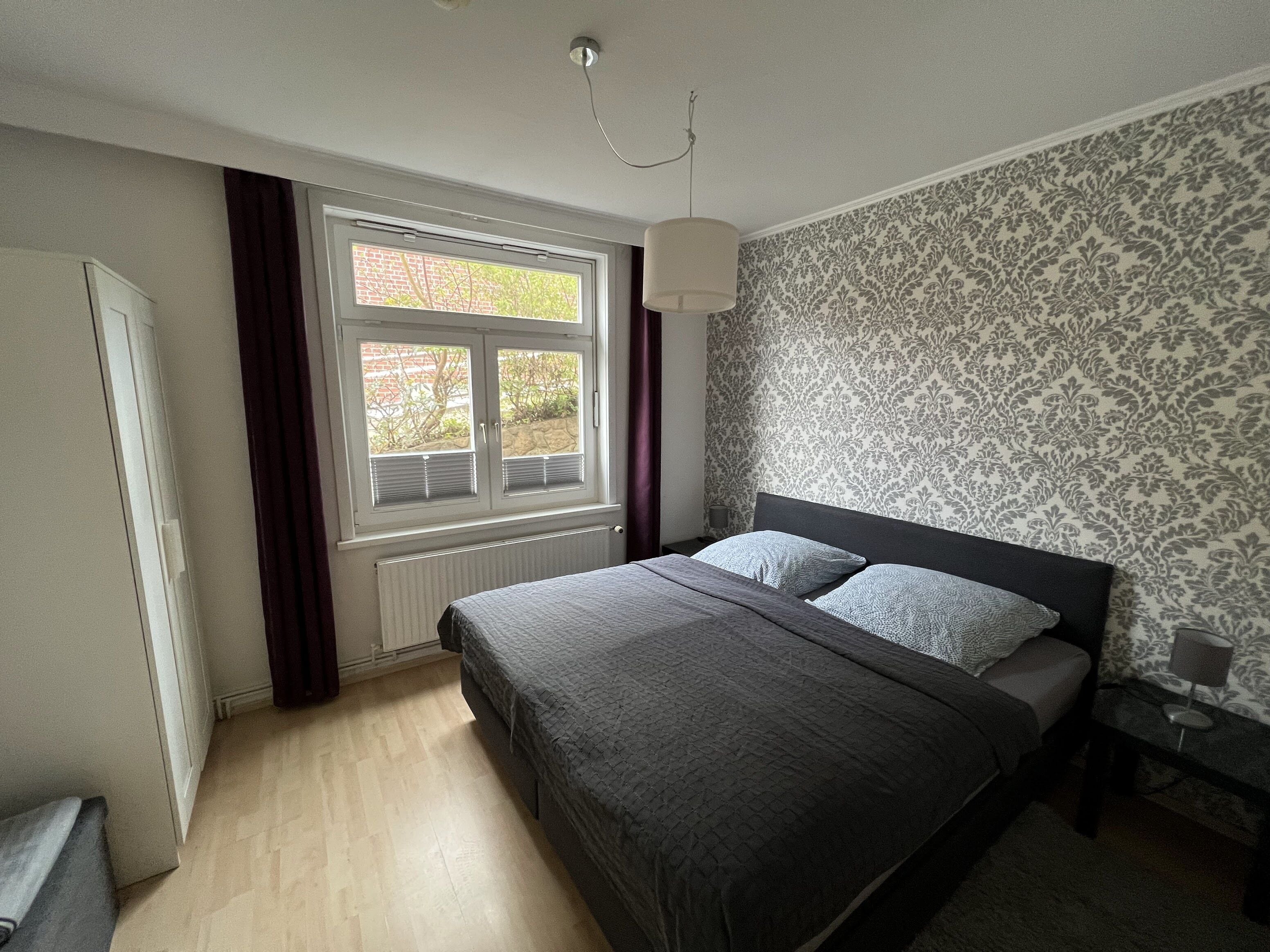 Un dormitorio con cama, ventana, radiador y pared decorada.