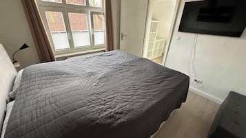 Un dormitorio con una cama grande, un televisor montado en la pared y una ventana con cortinas.